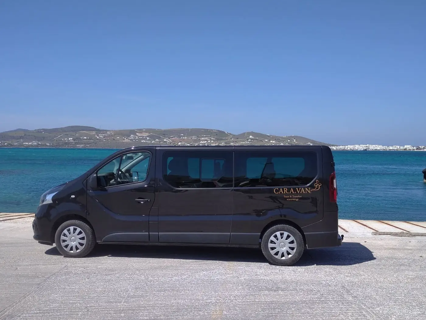 The Paros Tours van by the turquoise water on Paros, with Antiparos across the channel
